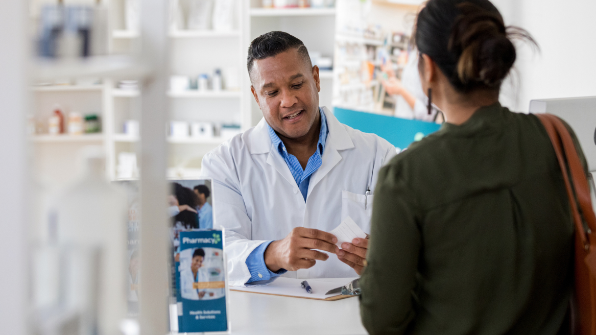 Pharmacist assisting a customer with medication at the pharmacy counter.