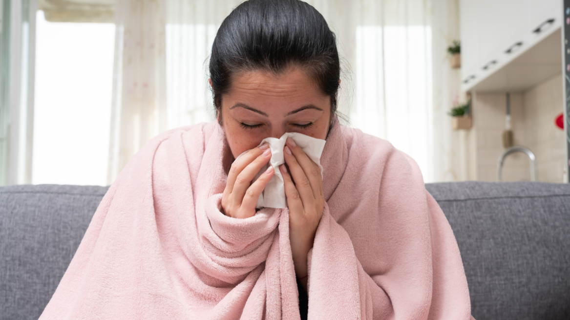 Woman wrapped in a blanket blowing her nose, showing symptoms of sinusitis.