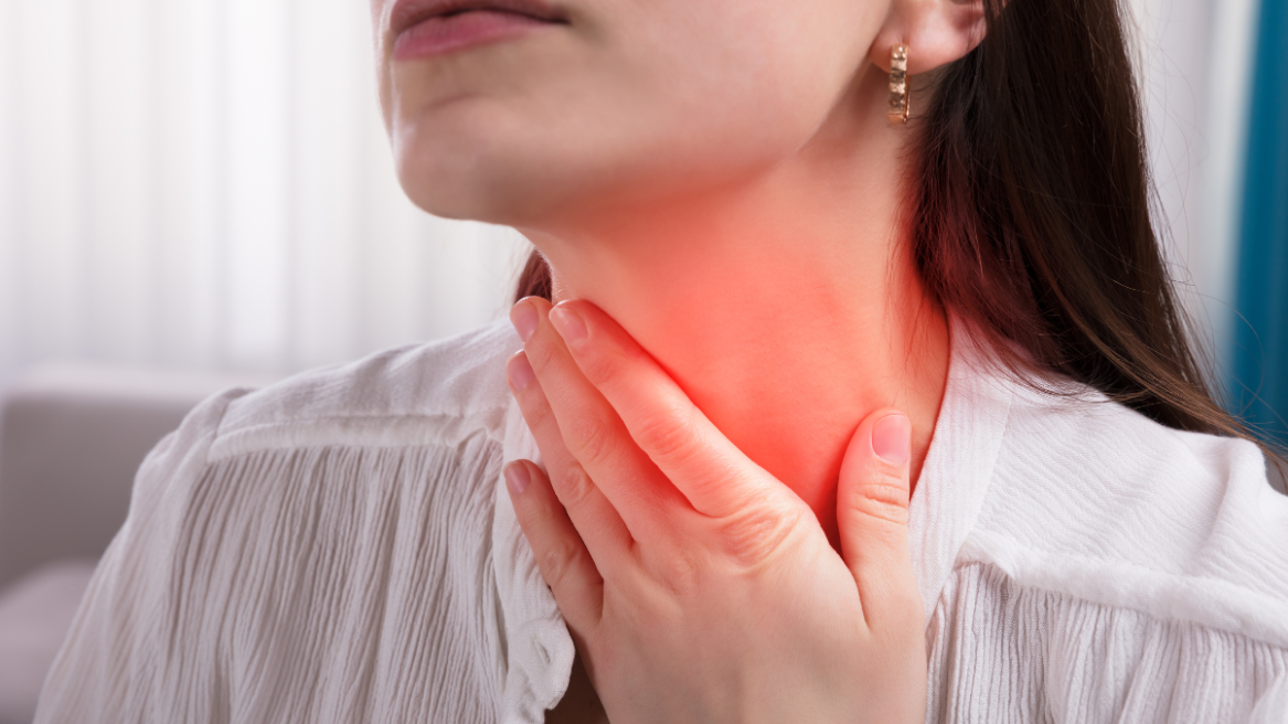 Adult touching their throat, showing visible discomfort from a sore throat.
